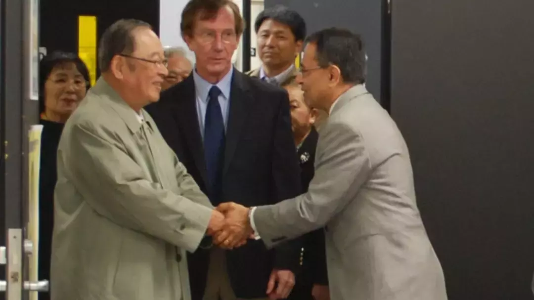 2 men in suits shaking hands in front of other men in suits