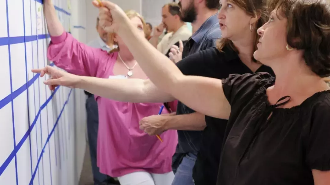 men and women pointing at a whiteboard with a grid on it